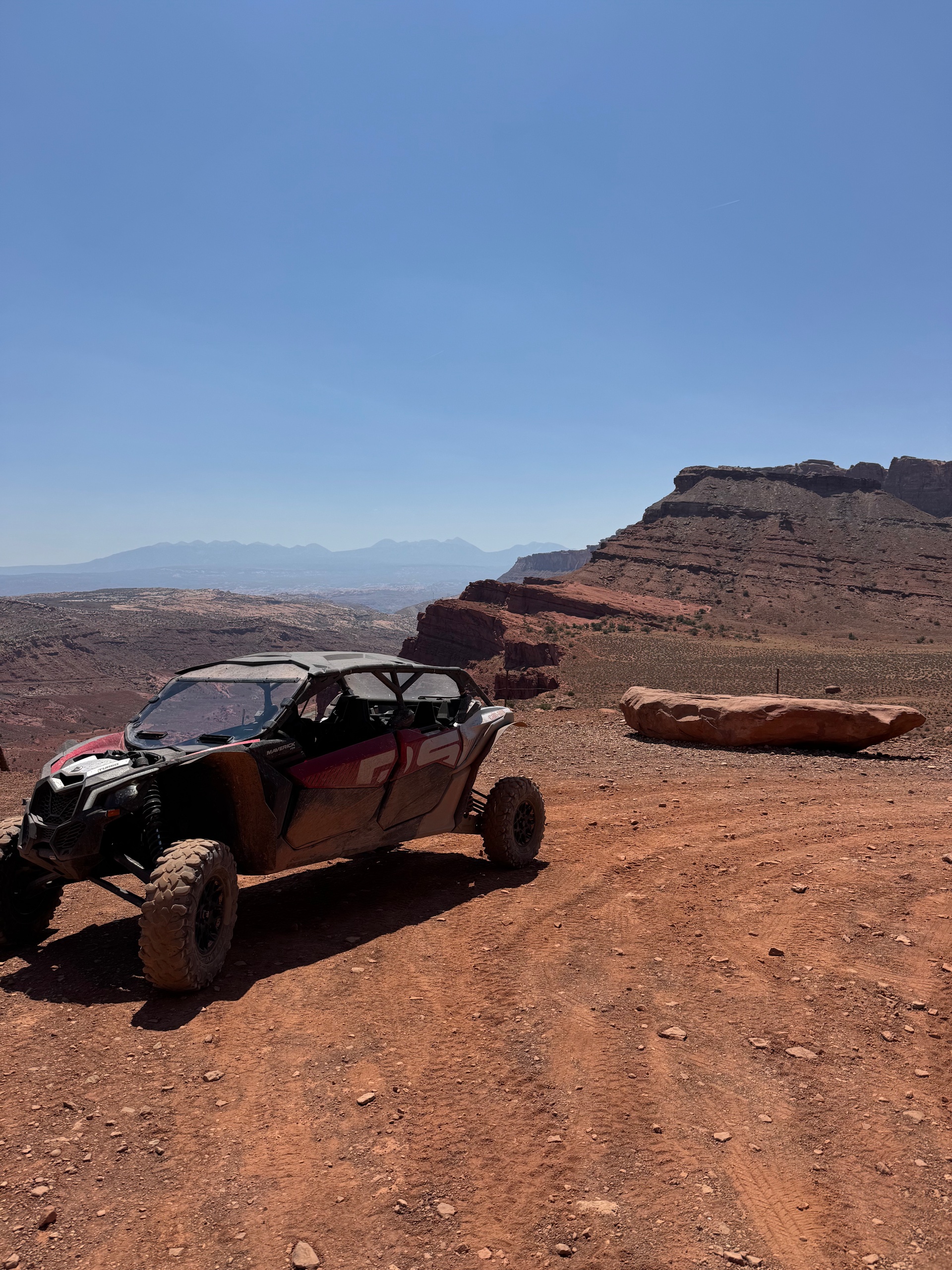 Off-road vehicle on dusty desert terrain with rocky landscape and blue sky.