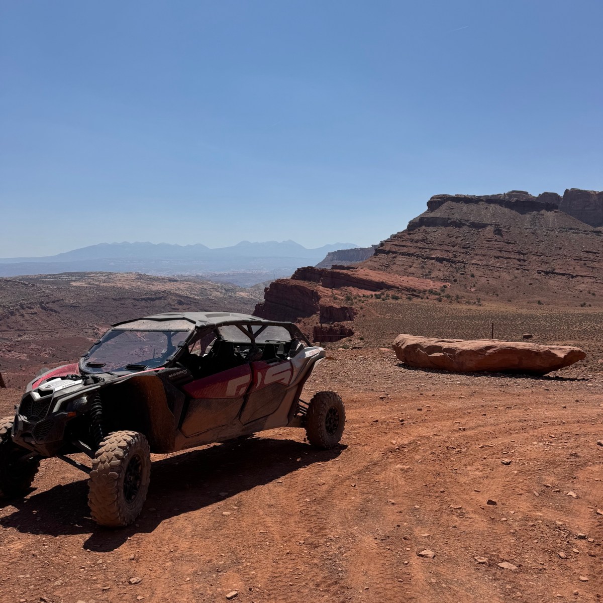 Off-road vehicle on dusty desert terrain with rocky landscape and blue sky.