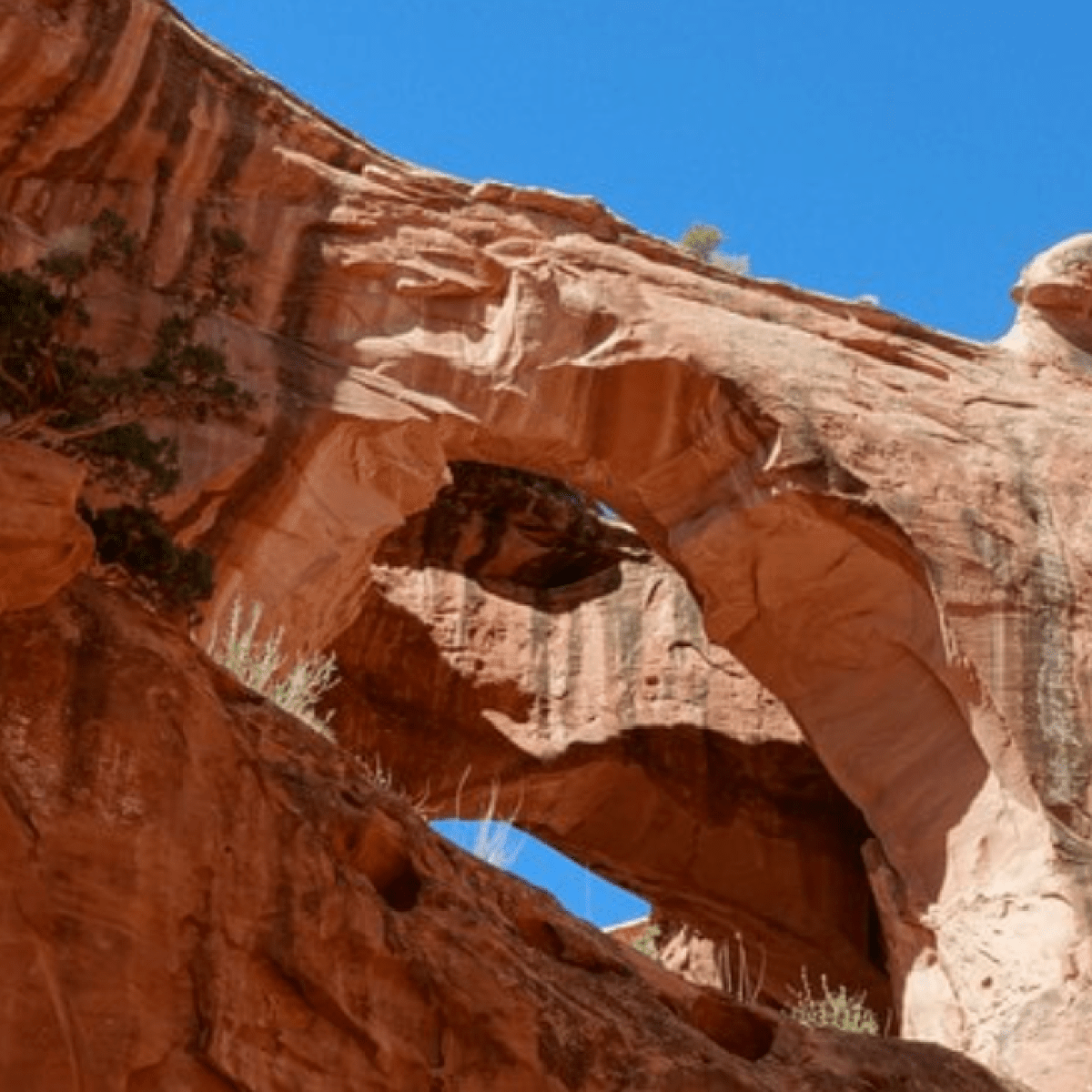 Rock arch with hole under clear blue sky, featuring red rock formations.