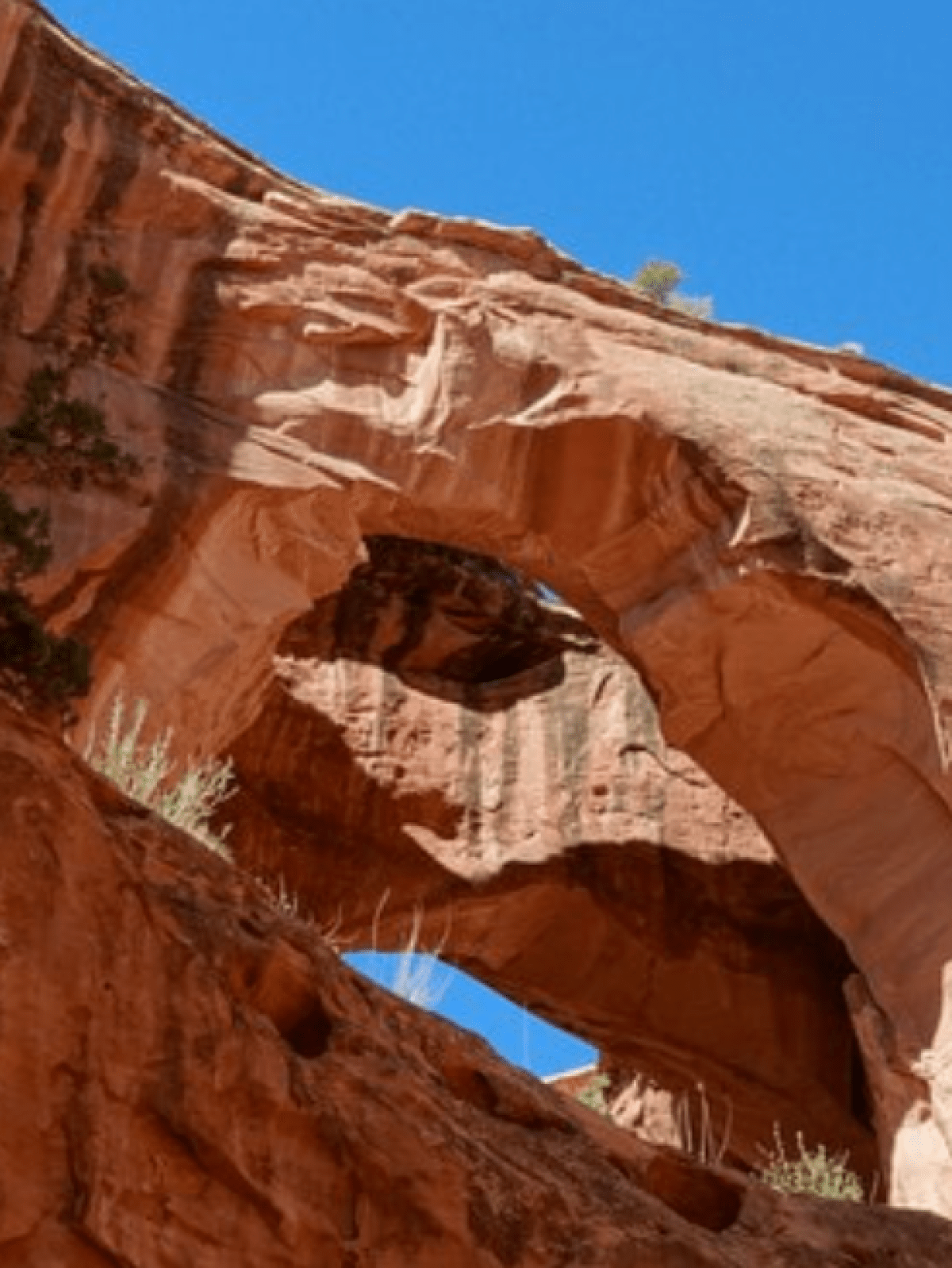 Rock arch with hole under clear blue sky, featuring red rock formations.