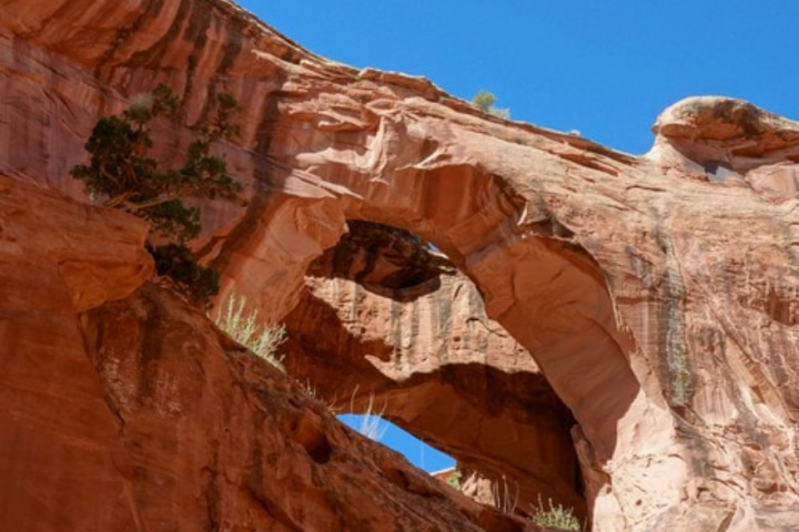 Rock arch with hole under clear blue sky, featuring red rock formations.