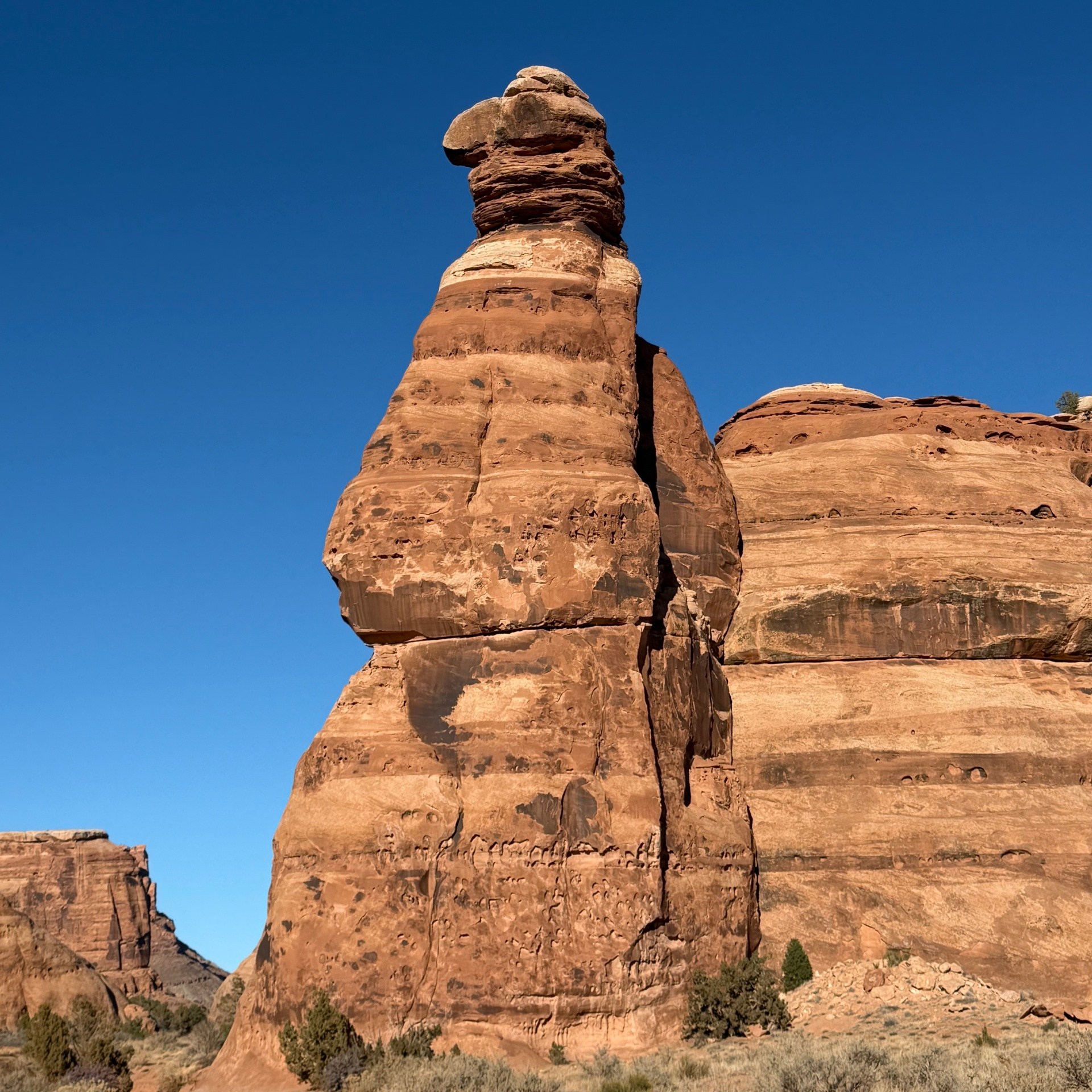 Tall sandstone rock formation under a clear blue sky in a desert landscape.