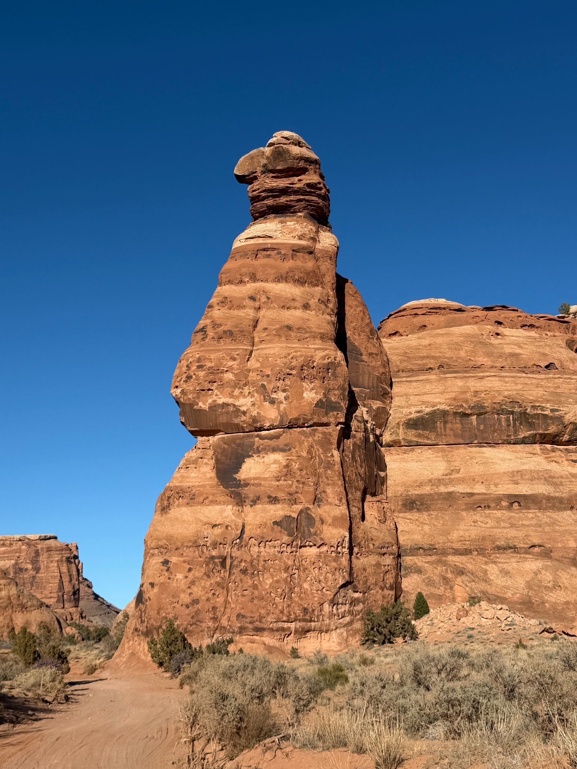 Tall sandstone rock formation under a clear blue sky in a desert landscape.