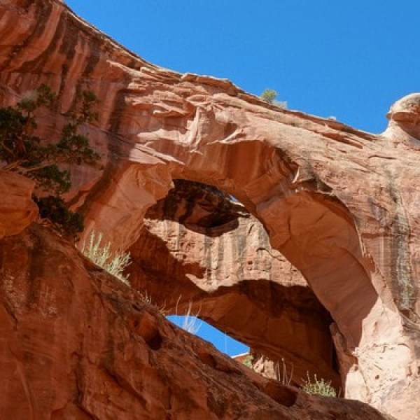 Natural red rock arch formation against a clear blue sky.
